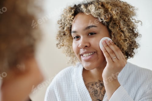 Preview: Young smiling woman applying makeup remover with cotton pad
