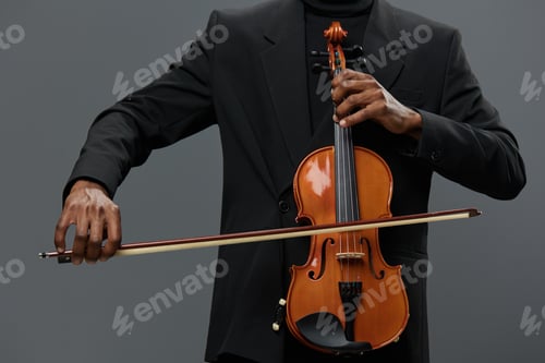 Preview: Elegant African American man in black suit holding a violin on gray background for music concept