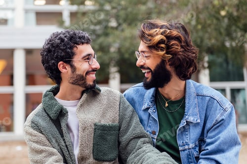 Preview: couple of gay men sitting in a park laughing happy