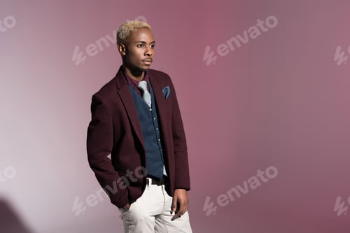 Preview: Young african man in red jacket standing with hand in pocket on pink background