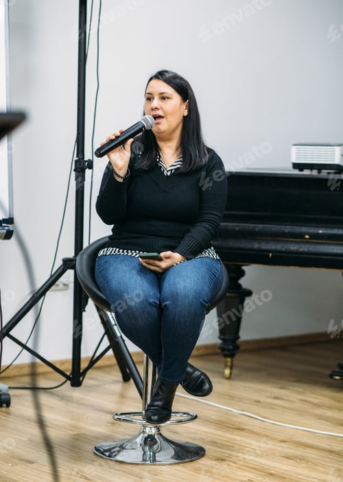 Preview: Young woman singing next to a piano. Rehearsing a song. Holding a microphone. Talking in public