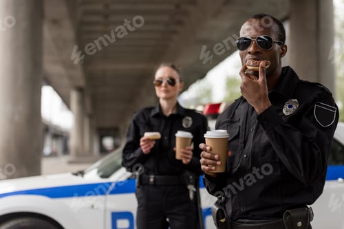 Preview: young police officers having coffee break with doughnuts in front of police car