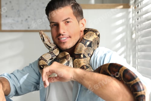 Preview: Man with his boa constrictor at home. Exotic pet