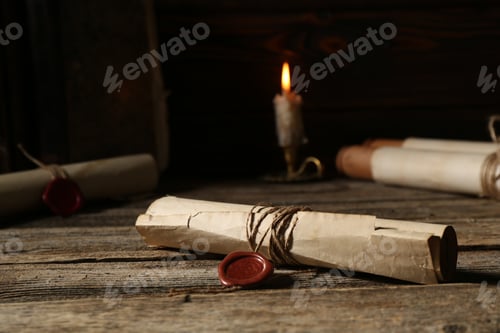 Preview: Old rolled paper scrolls and burning candle on wooden table, closeup