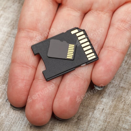 Preview: Memory cards on the palm of a young girl on a wooden table. Studio lighting. Close-up.