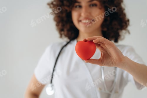 Preview: Red little heart toy in hands. Beautiful doctor woman is in the studio