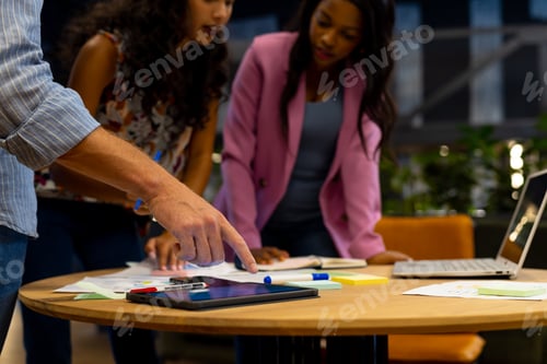 Preview: Diverse male and female colleagues in discussion using tablet and laptop in casual office meeting