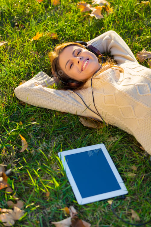 Preview: An attractive young woman listening to music on her digital tablet while outdoors