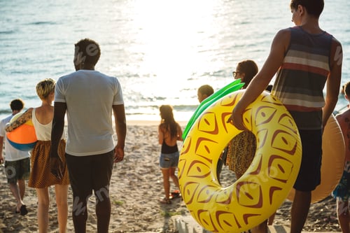 Preview: A diverse group of friends walking down to the beach with inflatable tubes