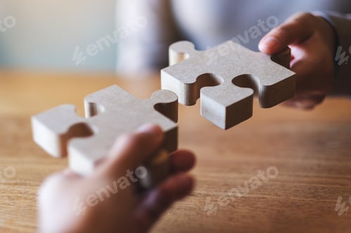 Preview: Closeup image of two people holding and putting a piece of wooden jigsaw puzzle together