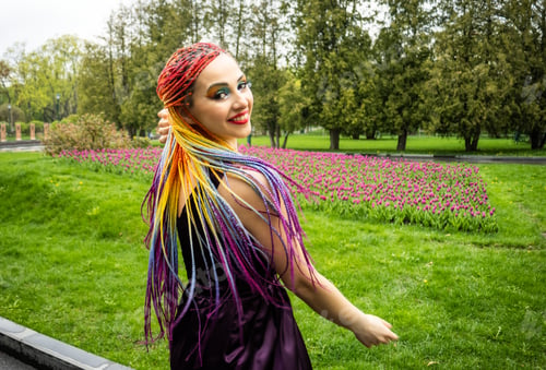 Preview: A girl in a purple dress and with rainbow long braids laughs and jumps in green blooming from the