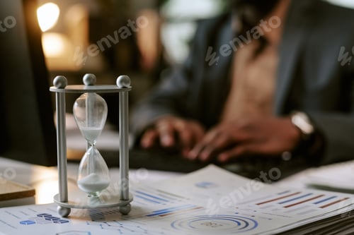 Preview: Middle Aged Black Man Working on Laptop with Hourglass in Office Setting