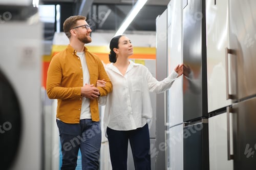 Preview: Young couple, satisfied customers choosing fridge in appliances store