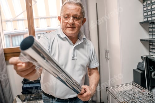 Preview: Portrait of positive senior man working in workshop, home office, holding tube, tool