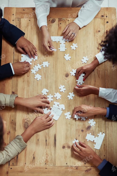 Preview: High angle shot of a group of unrecognisable businesspeople building a puzzle together