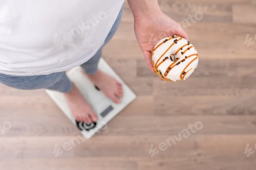 Preview: A woman stands on the scales, holds a donut in her hands, top view, copy space.