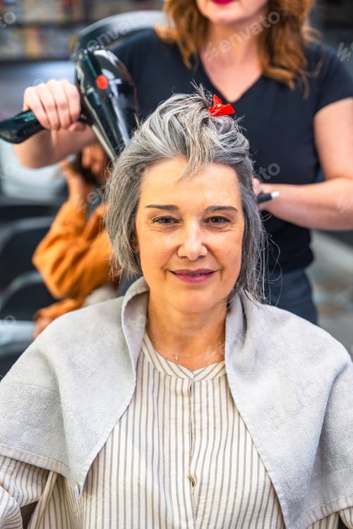 Preview: Woman blow drying hair seeing hairstylist in salon