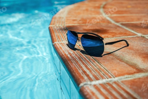 Preview: Sunglasses on side of pool with clear turquoise water. No people copy space