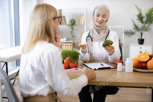 Preview: Arabian woman with fresh avocado in hand chatting with mature female lady.