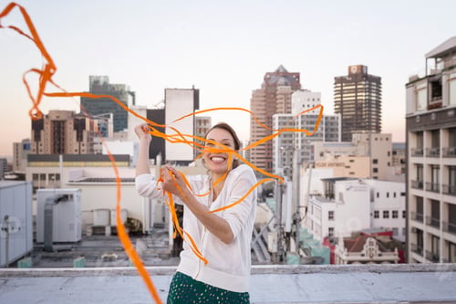 Preview: Young woman standing on a rooftop terrace, playing with a ribbon