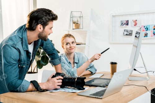 Preview: smiling young photographers discussing and retouching photos at workplace