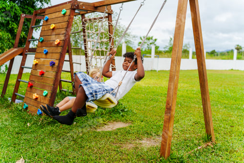 Preview: Two children play on swings, laughing and enjoying a sunny day at a lively park filled with grass