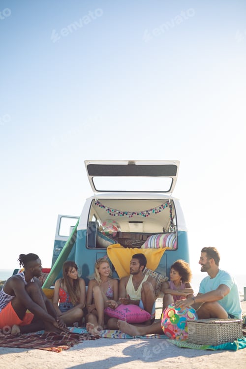 Preview: Front view of group of diverse friends interacting with each other near camper van at beach