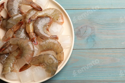 Preview: Fresh raw shrimps with ice cubes on light blue wooden table, top view. Space for text