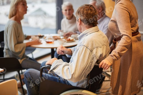 Preview: Man in wheelchair joining friends in cafe