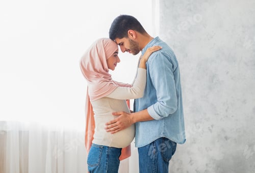 Preview: Romantic pregnant arab couple bonding, touching foreheads and smiling, standing near window, side