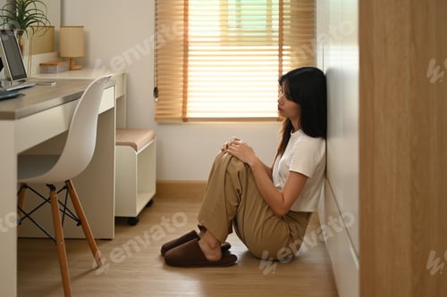 Preview: Sad and depressed young woman sitting alone on floor at home. Mental health concept