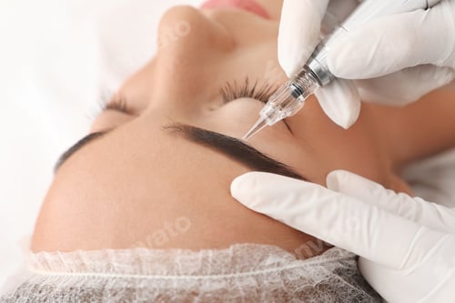 Preview: Young woman undergoing procedure of permanent eyebrow makeup in tattoo salon, closeup