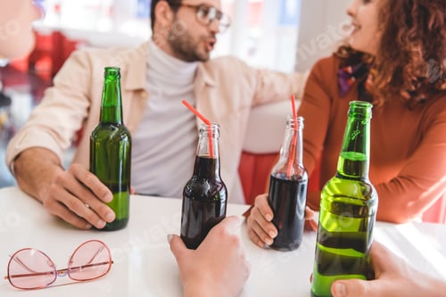 Preview: selective focus of glass bottles with drink holding by friends