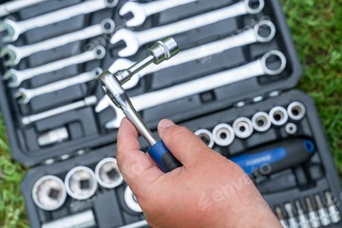 Preview: Man's hand holds a metal tool over a box with a set of tools supplies for construction work closeup