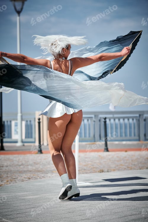 Preview: Young sexy girl in silver micro skirt dancing with performance fan waving gracefully, outdoor dance