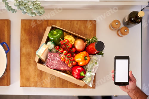 Preview: Hand In Kitchen Holding Phone With Blank Screen For Online Meal Food Recipe Kit Delivered To Home