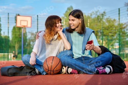Vista previa: Student friends sitting on outdoor basketball court looking in smartphone