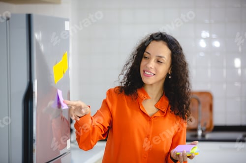 Preview: African female putting sticky note on refrigerator to remind her important job, work, plan