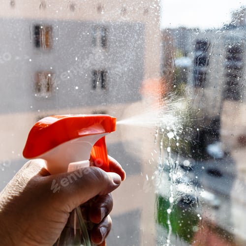 Preview: hand sprays washing liquid on window glass closeup