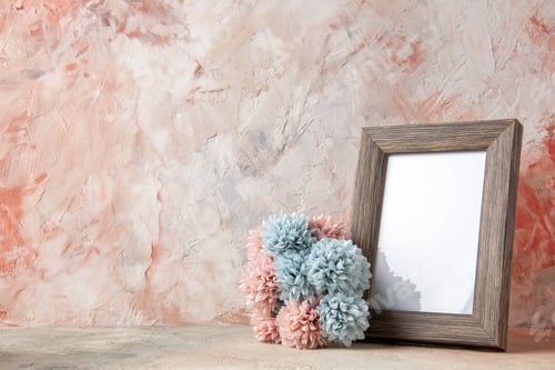 Preview: Top view of brown empty wooden photo frame standing on table and flower on the left side on nude