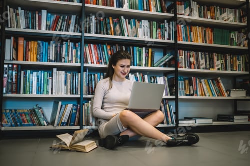 Preview: Smart woman smiling while working on laptop in library