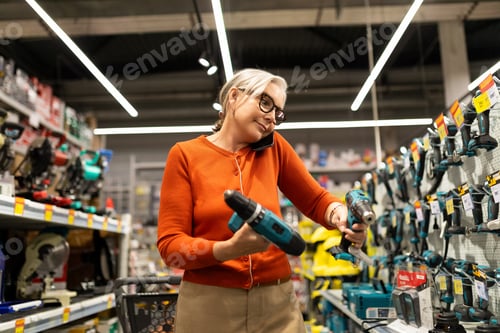 Preview: Woman shopping for power tools while talking on the phone in a hardware store during the day