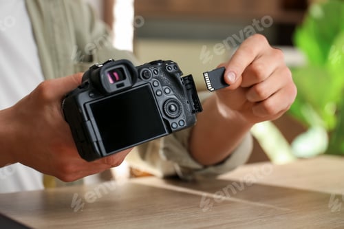 Preview: Man inserting SD memory card into photo camera at wooden table, closeup