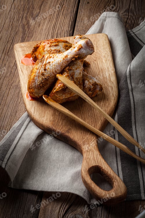 Preview: Marinated chicken drumsticks on a wooden chopping board.