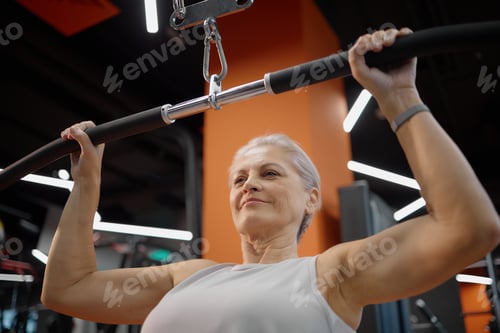 Preview: Senior Caucasian Woman Exercising on Pull down Machine at Modern Gym