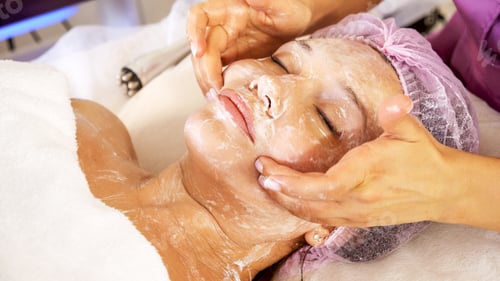 Preview: Cosmetologist applies a moisturizing mask on female face. Woman in a spa salon, cosmetic procedures