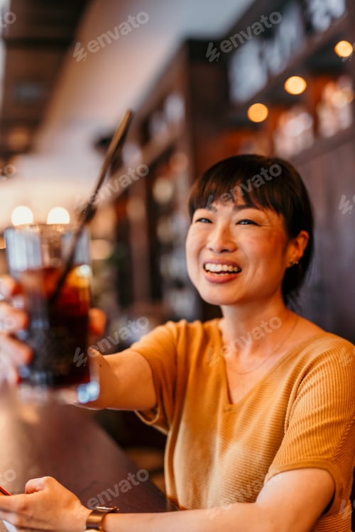 Preview: Happy woman toasting with a cold drink at the bar