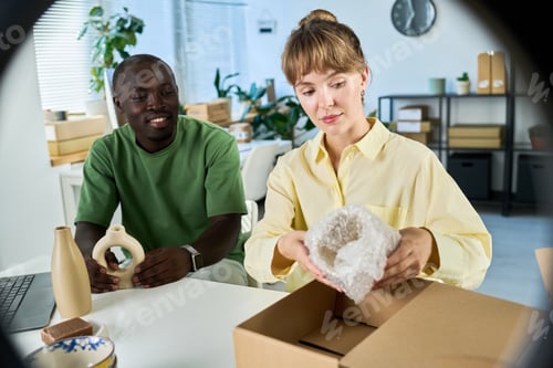 Preview: Young woman packing handmade vase wrapped in safety cellophane