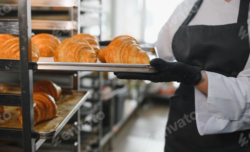 Preview: Baker holding tray of freshly baked croissants in bakery