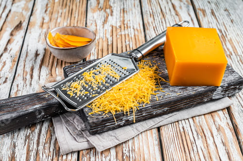 Preview: Grated Cheddar Cheese on a wooden cutting board. White wooden background. Top view